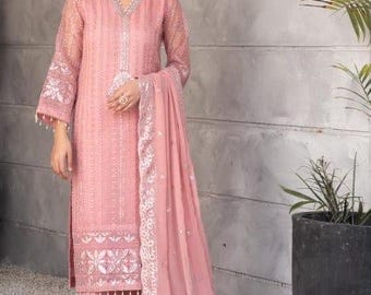May include: A woman wearing a pink embroidered dress with a matching pink dupatta. The dress has a long, flowing silhouette and features intricate floral embroidery. The dupatta is draped over the woman's shoulders and is also embroidered with floral designs.