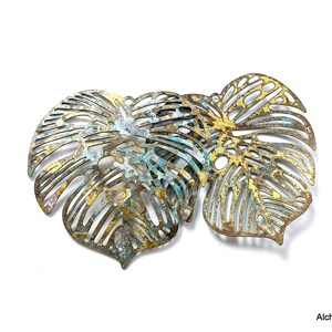 Könnte beinhalten: Nahaufnahme mehrerer metallener, blattförmiger Anhänger mit einem Used-Look-Finish. Die Blätter haben komplizierte Ausschnitte und eine Mischung aus Gold-, Blau- und Bronzetönen. Die Anhänger sind wahrscheinlich für die Schmuckherstellung oder andere Bastelprojekte gedacht.