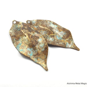 May include: Two leaf-shaped metal pendants with a textured, marbled finish in shades of brown, gold, and turquoise.