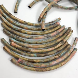 May include: A selection of curved copper tubes, displaying a weathered patina with shades of brown, green, and pink. The open-ended tubes suggest a hollow interior. These craft components could be used for jewellery making or other creative projects. The tubes are likely measured in centimeters.