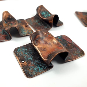 May include: Four copper metal pieces with a turquoise patina. The pieces are rectangular and have been folded and bent to create a unique shape. The metal has a textured surface.