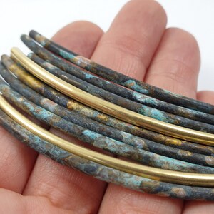 May include: A close-up of a stack of round, brass wire with a blue-green patina. The wire is arranged in a semi-circle, with the top wire being a solid brass colour.