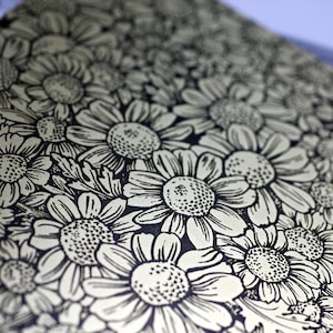 May include: A close-up of a black and white floral pattern on a cream background. The pattern is made up of repeating daisy-like flowers.