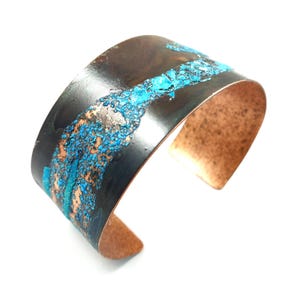 May include: Wide copper cuff bracelet with a dark patina and turquoise accents. The bracelet has a textured surface with a unique, artistic design. The open cuff design allows for easy wear.