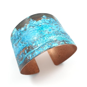 May include: Wide copper cuff bracelet with a turquoise and brown patina. The open cuff design features a textured surface with a weathered appearance. The bracelet is approximately 2 inches wide.