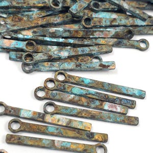 May include: A pile of turquoise, brown, and gold metal bar pendants with a small loop at one end. The pendants have a marbled, textured finish.