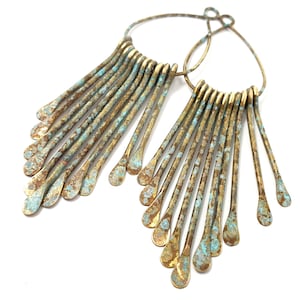 May include: A pair of large hoop earrings with a fringe of thin, gold-toned metal strands. The strands have a distressed, aged finish with a turquoise patina.