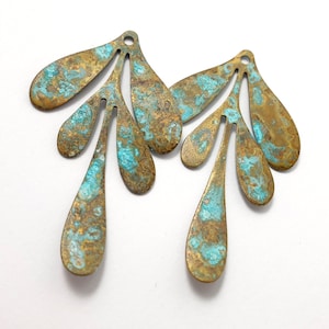 May include: Two antique brass leaf-shaped charms with a distressed turquoise finish. The charms have a hole at the top for hanging.