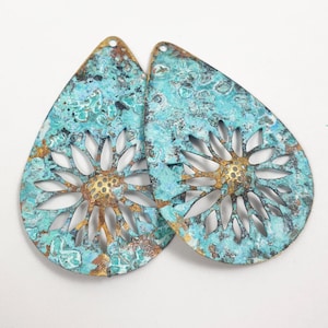 May include: Two teal blue and gold metal teardrop-shaped earrings with a cut-out floral design. The earrings have a distressed, aged look.