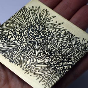 May include: A square metal plaque with a black and white etched design of pine cones and branches.