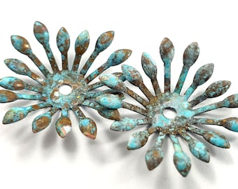 May include: Two turquoise blue metal flower-shaped embellishments with a distressed finish. Each embellishment has a center hole and multiple pointed petals.
