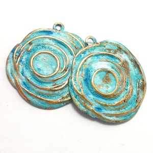 May include: Two turquoise and gold metal swirl pendant charms with a textured finish.