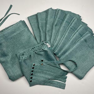 May include: A set of teal linen curtains with a tie-back feature and metal grommets. The curtains are made of a soft, textured fabric and have a relaxed, casual look.