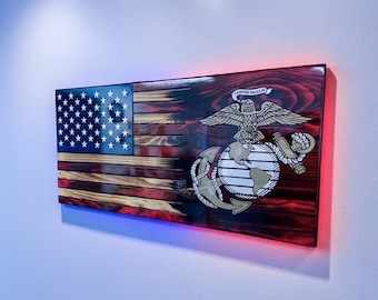 May include: A rectangular wooden wall plaque featuring a charred American flag design with a blue canton of white stars and red and white stripes. The United States Marine Corps emblem, featuring an eagle, globe, and anchor, is centered on the right.