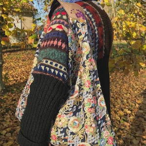 May include: A colorful, patterned shoulder bag with a floral design and black sleeves. The bag features a mix of knitted and printed fabrics, with a brown leather shoulder strap. The design includes various colors, including blue, green, red, and white.