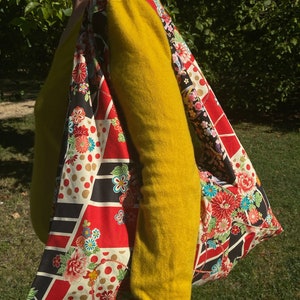 May include: A large tote bag with a colorful floral and geometric pattern. The bag features red, black, and white panels with floral designs and gold polka dots. The strap is wide and made of the same patterned fabric.