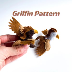 Pode incluir: Duas pequenas figuras de grifo em feltro com o texto Griffin Pattern acima. Um grifo é castanho escuro com asas bege, e o outro é branco com asas castanhas e bege. Ambos apresentam detalhes costurados, orelhas pontiagudas e bicos amarelos.