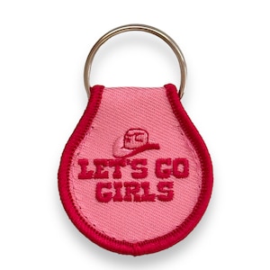 Puede incluir: Llavero de tela rosa con un sombrero vaquero bordado en rojo y el texto "Let's Go Girls".