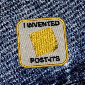 May include: A yellow and white embroidered patch with the text "I invented Post-its" and a yellow sticky note illustration.