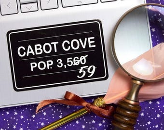 May include: A black and white sign with the text "CABOT COVE POP. 3,560 59" on a silver laptop. A magnifying glass and a feather pen are on a purple background with white stars.