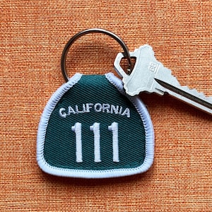 May include: A green and white key chain with the text "CALIFORNIA 111" on it. The key chain is attached to a silver key.