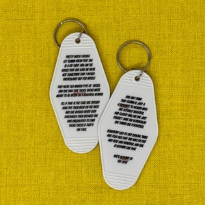 May include: Two white motel-style keychains with black text on a yellow background. The keychains have a rounded rectangular shape and a metal ring. The text on the keychains is a poem about shoes and beauty.