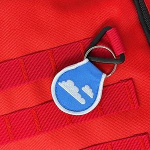 May include: A red backpack with a blue and white cloud-shaped keychain attached to a black zipper pull.