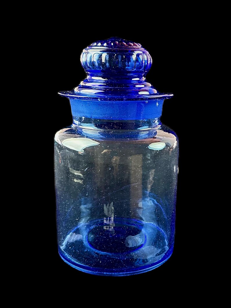 Peut inclure: Un bocal d'apothicaire en verre bleu cobalt avec un couvercle assorti. Le bocal a une base large et un corps cylindrique, avec un bord &eacute;vas&eacute; et un couvercle d&eacute;coratif et arrondi. Le verre est transparent.
