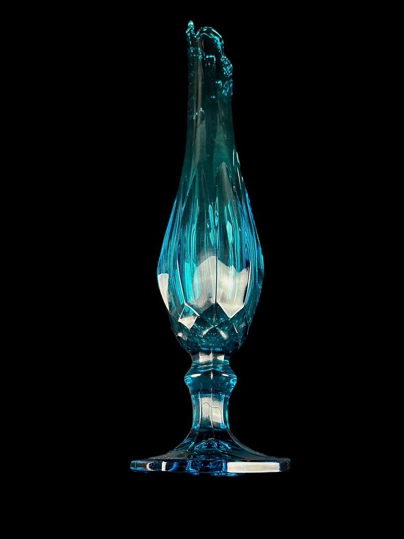 Pode incluir: Um vaso de vidro azul alto com uma base alargada e uma parte superior com babados. O vaso tem um design texturizado e facetado.