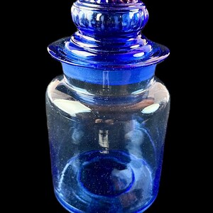 Peut inclure: Un pot de pharmacie en verre bleu cobalt avec un couvercle assorti. Le pot est cylindrique avec une base arrondie et un bord &eacute;vas&eacute;. Le couvercle est de forme arrondie avec un bouton sur le dessus. Le pot est vide.