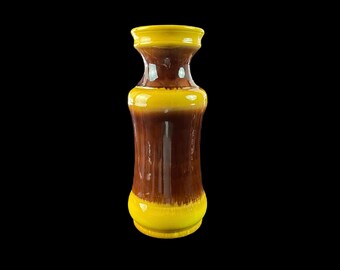 May include: A brown and yellow ceramic vase with a flared top and a rounded bottom. The vase has a glazed finish and a unique color pattern.