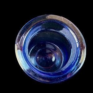Peut inclure: Vue de dessus d'un objet en verre bleu de forme circulaire. L'objet est d'un bleu profond et sombre, avec des reflets bleus clairs sur le bord. L'int&eacute;rieur r&eacute;v&egrave;le des cercles concentriques, cr&eacute;ant une sensation de profondeur sur fond noir.