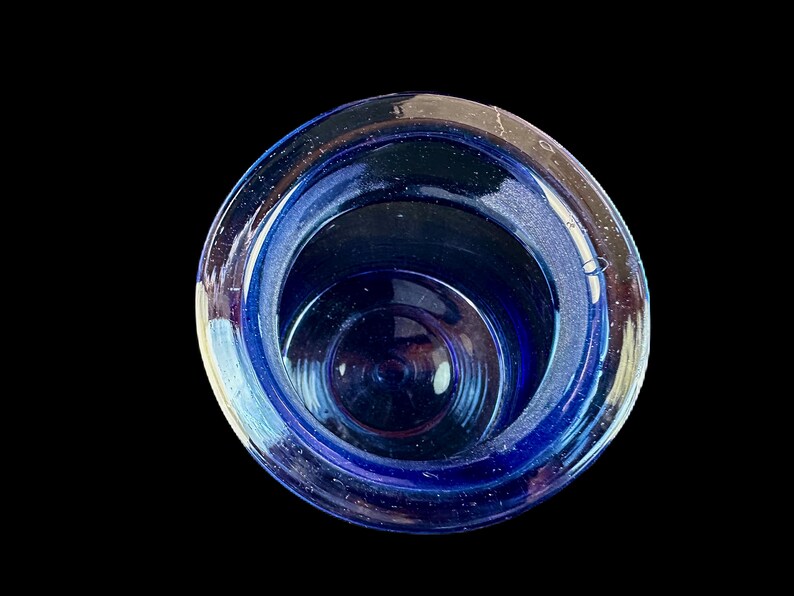 Peut inclure: Vue de dessus d'un objet en verre bleu de forme circulaire. L'objet est d'un bleu profond et sombre, avec des reflets bleus clairs sur le bord. L'int&eacute;rieur r&eacute;v&egrave;le des cercles concentriques, cr&eacute;ant une sensation de profondeur sur fond noir.