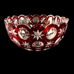 May include: A red glass bowl with a cut glass design of stars and circles. The bowl is clear glass with a red overlay.
