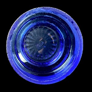 Peut inclure: Vue de dessus d'un objet en verre bleu cobalt de forme circulaire. L'objet a un bord textur&eacute; et un int&eacute;rieur d&eacute;taill&eacute; et nervur&eacute;. Le verre semble transparent, la lumi&egrave;re se refl&eacute;tant &agrave; travers le centre. Le fond est noir uni.