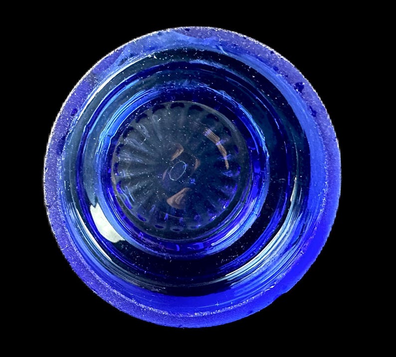 Peut inclure: Vue de dessus d'un objet en verre bleu cobalt de forme circulaire. L'objet a un bord textur&eacute; et un int&eacute;rieur d&eacute;taill&eacute; et nervur&eacute;. Le verre semble transparent, la lumi&egrave;re se refl&eacute;tant &agrave; travers le centre. Le fond est noir uni.