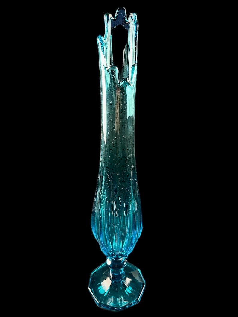 Pode incluir: Um vaso de vidro azul alto com um design ondulado &uacute;nico. O vaso tem uma base larga e alargada e um pesco&ccedil;o estreito.