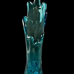 Pode incluir: Um vaso de vidro azul alto com uma forma org&acirc;nica &uacute;nica. O vaso &eacute; feito de vidro transparente com um tom azul e tem um design ondulado e fluido.