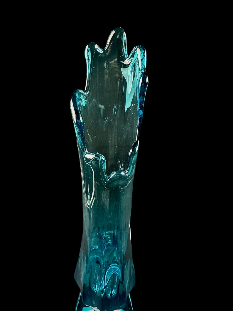 Pode incluir: Um vaso de vidro azul alto com uma forma org&acirc;nica &uacute;nica. O vaso &eacute; feito de vidro transparente com um tom azul e tem um design ondulado e fluido.
