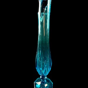 Pode incluir: Um vaso de vidro azul alto com uma base octogonal alargada e uma parte superior ondulada e texturizada.