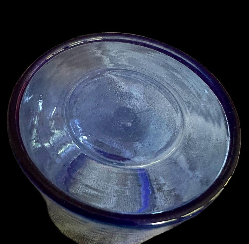 Peut inclure: Gros plan d'un objet en verre bleu, possiblement un verre ou un bol, sur fond noir. Le bord est d'une nuance de bleu plus fonc&eacute;e, et l'int&eacute;rieur a un aspect l&eacute;g&egrave;rement givr&eacute;.