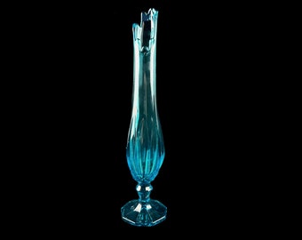 Peut inclure: Un vase en verre bleu clair, haut et évasé, avec un motif texturé et facetté. Le vase a une base large et octogonale.