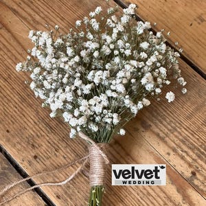 Op de afbeelding: Een boeket witte gipskruidbloemen, vastgebonden met touw. De stelen zijn omwikkeld met touw en de bloemen zijn gegroepeerd. De achtergrond is een houten oppervlak. De tekst "velvet WEDDING" is zichtbaar.