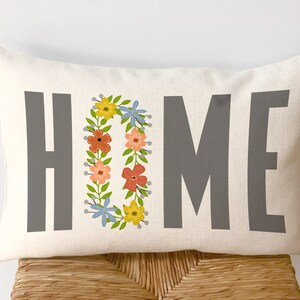 May include: A white pillow with the word "HOME" in gray text. The "O" in home is a wreath of colorful flowers.