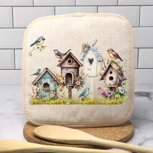 May include: A beige linen pot holder with a colorful design of birdhouses and bluebirds. The birdhouses are decorated with flowers and have heart-shaped windows.