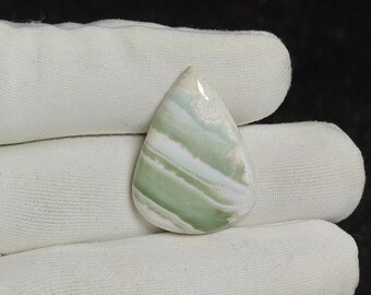 May include: A teardrop-shaped cabochon gemstone featuring alternating bands of pale mint green and opaque white. The stone has a smooth, polished surface with a glossy finish, displaying a natural layered pattern throughout its entire structure.