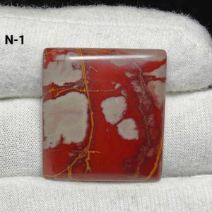 May include: Square gemstone with a polished surface. The stone has a vibrant red base colour with white and cream-coloured patterns and golden-yellow veins. The text "N-1" is visible in the upper left corner.