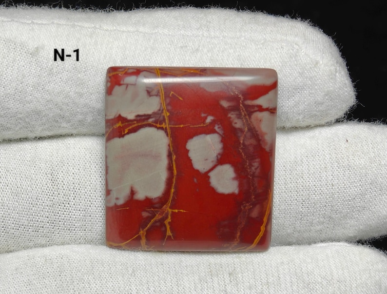 May include: Square gemstone with a polished surface. The stone has a vibrant red base colour with white and cream-coloured patterns and golden-yellow veins. The text "N-1" is visible in the upper left corner.