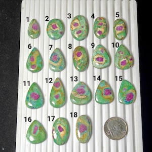 Peut inclure: Une collection de dix-huit pierres précieuses polies de formes variées, dont ovales, en forme de goutte et triangulaires. Les pierres présentent des teintes vertes, roses et jaunes. Une pièce de monnaie est incluse pour la comparaison des tailles.