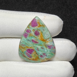 May include: A teardrop-shaped gemstone with a turquoise base colour, featuring vibrant magenta and orange inclusions. The polished stone is held in a white gloved hand, showcasing its natural patterns and textures.